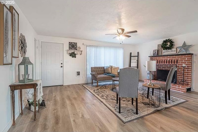 living area with light wood-style floors, a brick fireplace, baseboards, and a ceiling fan