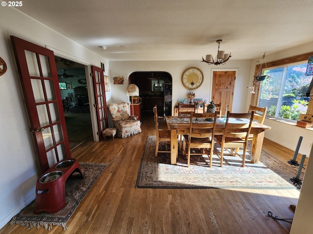 dining space with a chandelier, wood-type flooring, arched walkways, and baseboards