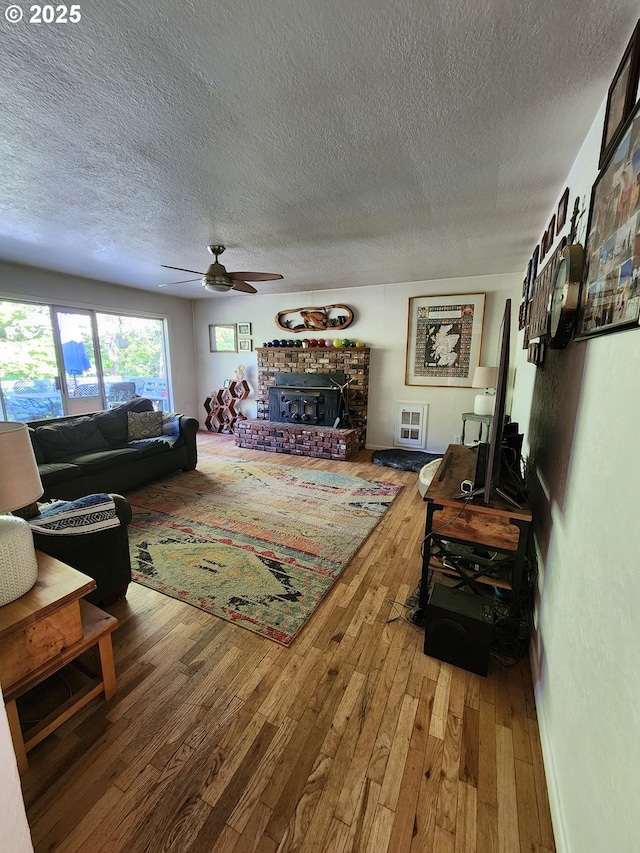 living area with wood finished floors, a textured ceiling, ceiling fan, and a fireplace