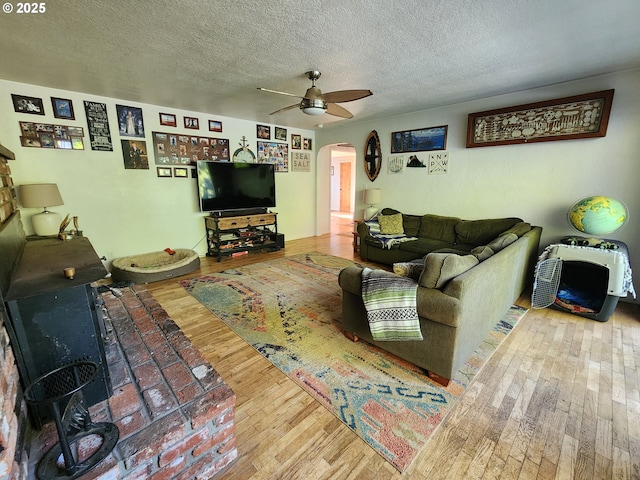 living area featuring arched walkways, ceiling fan, hardwood / wood-style flooring, and a textured ceiling