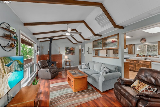 living room featuring visible vents, lofted ceiling with skylight, light wood-style flooring, ceiling fan, and a wood stove