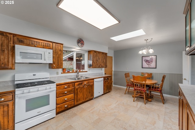 kitchen featuring white appliances, brown cabinetry, a sink, light countertops, and wainscoting