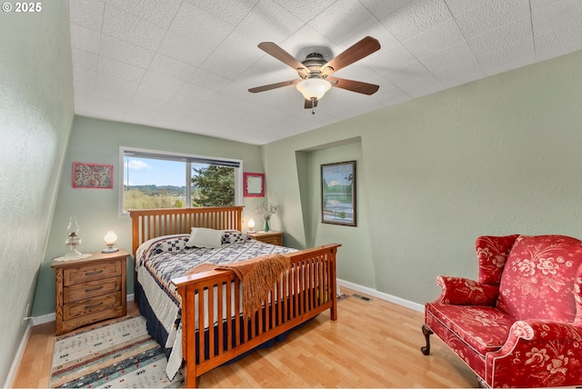 bedroom with ceiling fan, baseboards, wood finished floors, and a textured wall