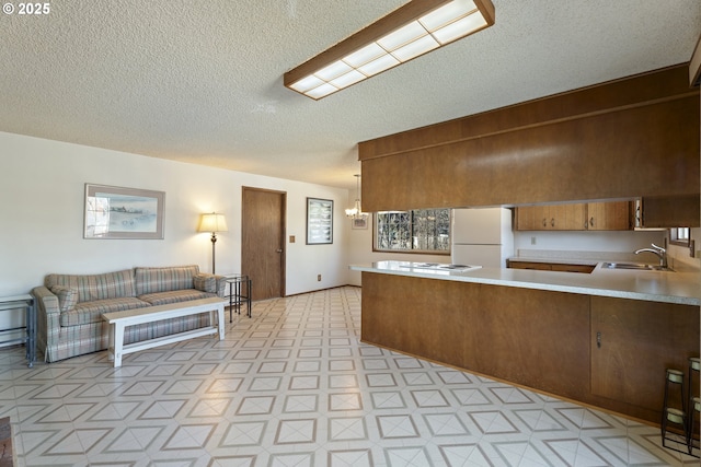 kitchen with sink, an inviting chandelier, decorative light fixtures, white refrigerator, and kitchen peninsula