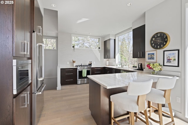 3701 SW 38th Ave, Portland, OR 97221 - kitchen featuring stainless steel appliances, a peninsula, a kitchen breakfast bar, tasteful backsplash, and light wood-style floors