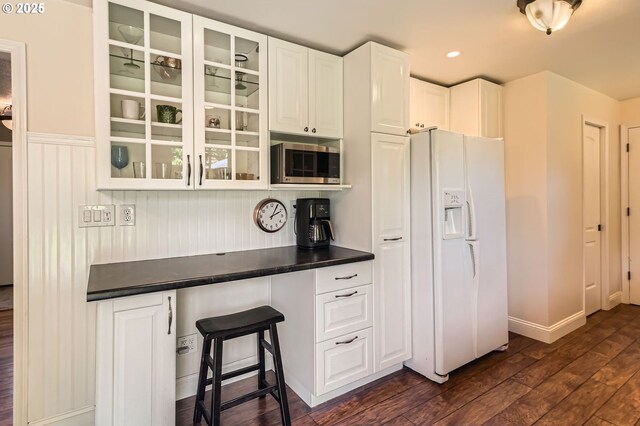 kitchen featuring dark countertops, glass insert cabinets, dark wood-style floors, stainless steel microwave, and white fridge with ice dispenser