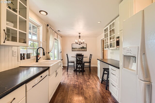 kitchen with dark countertops, a sink, dark wood-style floors, a notable chandelier, and white appliances