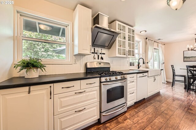 kitchen with white dishwasher, dark countertops, gas stove, a sink, and wall chimney exhaust hood