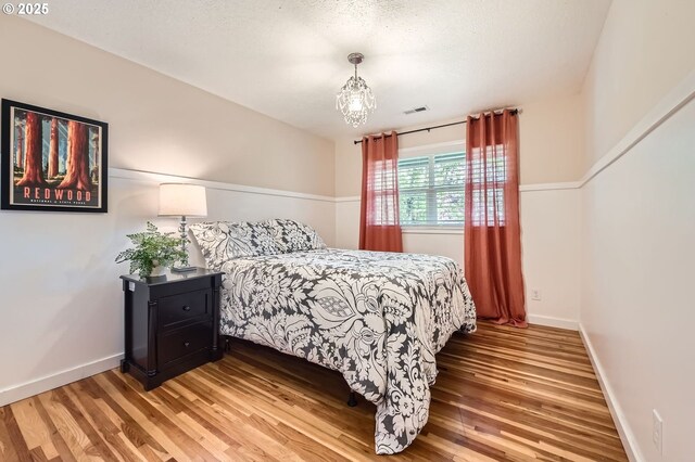 bedroom featuring light wood-type flooring, baseboards, visible vents, and an inviting chandelier