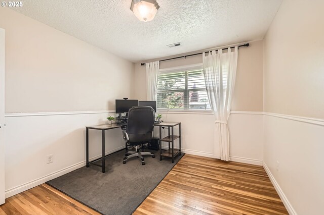 office space with visible vents, baseboards, a textured ceiling, and wood finished floors