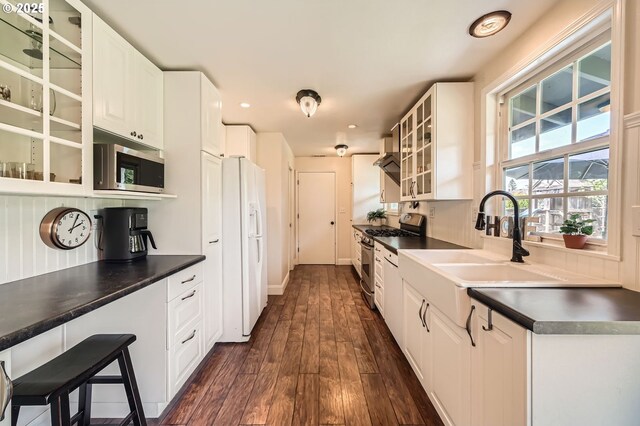 kitchen featuring dark countertops, appliances with stainless steel finishes, a sink, white cabinetry, and dark wood-style floors