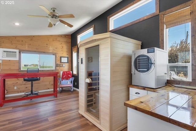 interior space featuring stacked washer / drying machine, wooden walls, wood finished floors, a wall unit AC, and ceiling fan
