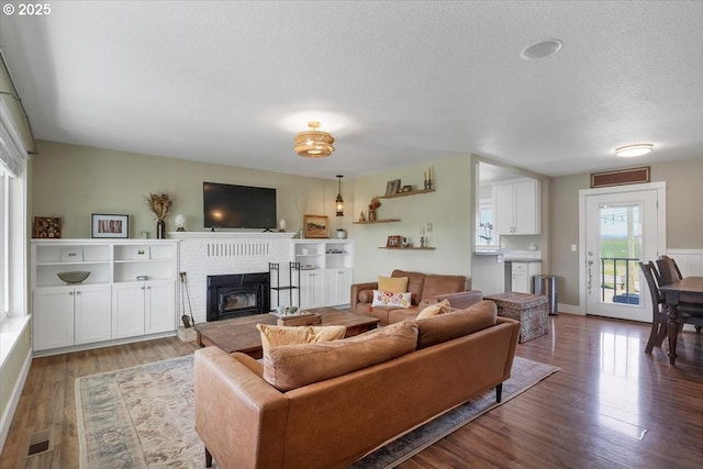 living room with a textured ceiling, wood finished floors, visible vents, and a brick fireplace