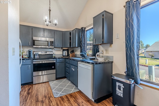 kitchen featuring vaulted ceiling, appliances with stainless steel finishes, gray cabinetry, dark hardwood / wood-style flooring, and hanging light fixtures