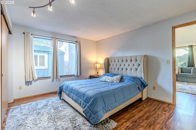 bedroom featuring dark hardwood / wood-style flooring, a textured ceiling, and rail lighting