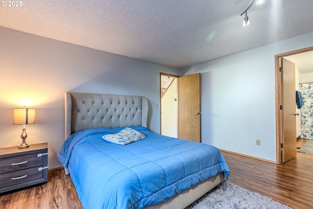 bedroom featuring dark hardwood / wood-style flooring, a textured ceiling, and rail lighting