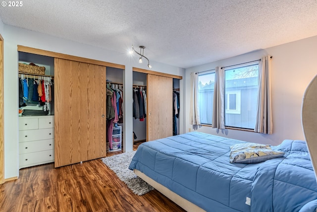 bedroom featuring dark wood-type flooring, multiple closets, and a textured ceiling