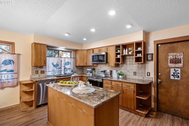 kitchen featuring sink, a center island, light wood-type flooring, stainless steel appliances, and light stone countertops