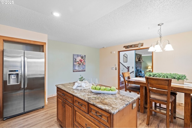 kitchen with pendant lighting, light hardwood / wood-style flooring, stainless steel refrigerator with ice dispenser, light stone countertops, and a kitchen island