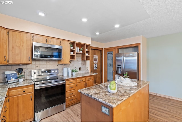 kitchen featuring appliances with stainless steel finishes, tasteful backsplash, a center island, light stone counters, and light wood-type flooring