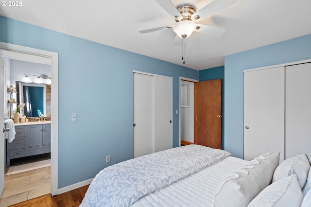 bedroom featuring hardwood / wood-style floors, two closets, sink, ceiling fan, and ensuite bath