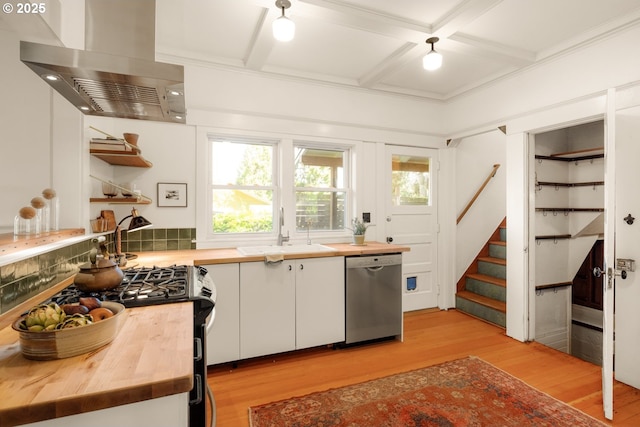 kitchen with wall chimney range hood, wooden counters, a sink, and dishwasher