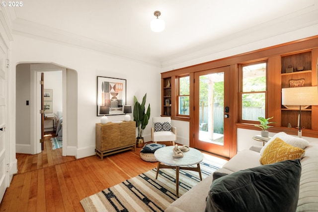 living room with light wood-style floors, arched walkways, baseboards, and ornamental molding