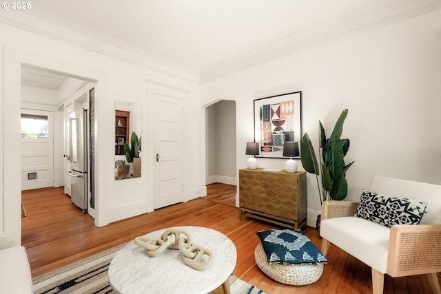 living area featuring arched walkways, ornamental molding, and light wood-type flooring