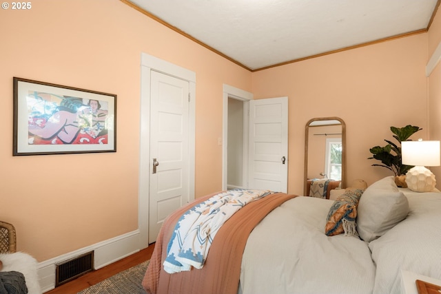 bedroom featuring baseboards, ornamental molding, wood finished floors, and visible vents