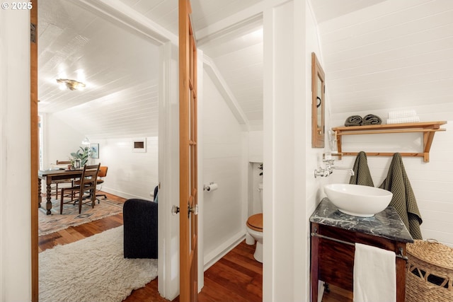 bathroom featuring vanity, wood finished floors, toilet, baseboards, and vaulted ceiling