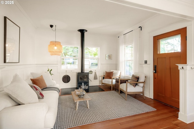 living room featuring crown molding, a wood stove, wainscoting, a decorative wall, and wood finished floors