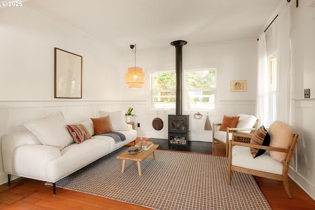 interior space featuring a wainscoted wall, a wood stove, wood finished floors, and ornamental molding
