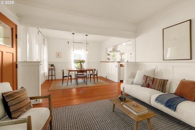 living room with ornamental molding, wainscoting, wood finished floors, and a decorative wall