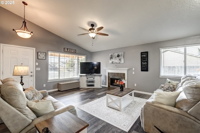 living area with a wealth of natural light, dark wood-style flooring, vaulted ceiling, and a tile fireplace