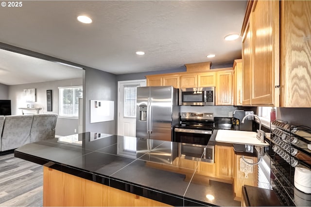 kitchen with tile countertops, stainless steel appliances, light wood-style flooring, open floor plan, and a peninsula