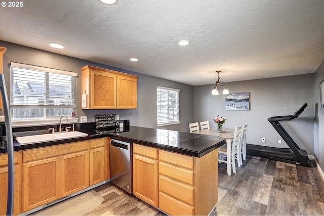 kitchen featuring a textured ceiling, a peninsula, wood finished floors, a sink, and dishwasher