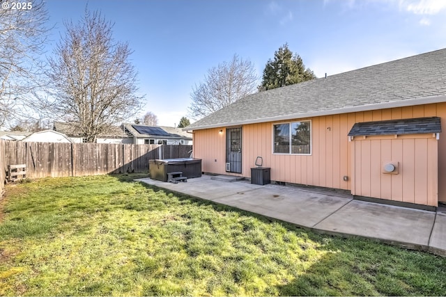 back of property with roof with shingles, a patio, a lawn, a hot tub, and a fenced backyard