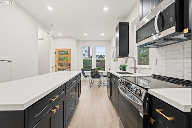 kitchen with light hardwood / wood-style flooring, sink, backsplash, a kitchen island, and stainless steel appliances