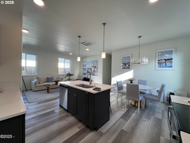 kitchen with a sink, appliances with stainless steel finishes, dark cabinetry, wood finished floors, and light countertops