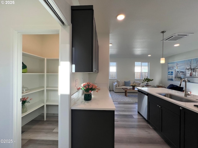kitchen with dishwasher, a sink, dark cabinetry, open floor plan, and light countertops