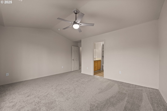 unfurnished bedroom featuring a ceiling fan, light carpet, vaulted ceiling, ensuite bath, and baseboards