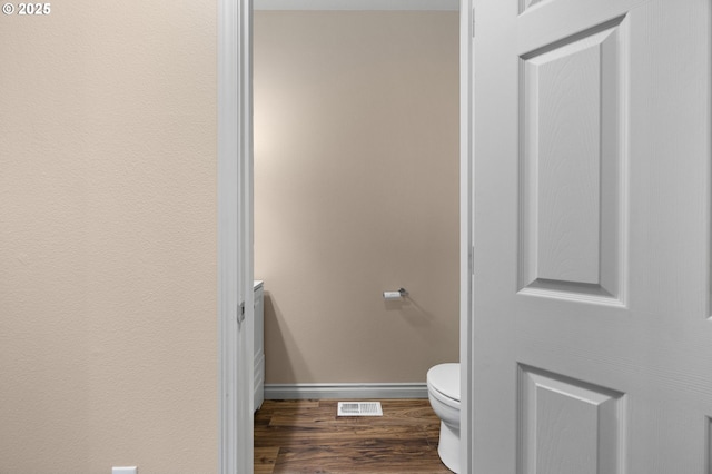 bathroom with baseboards, visible vents, toilet, and wood finished floors