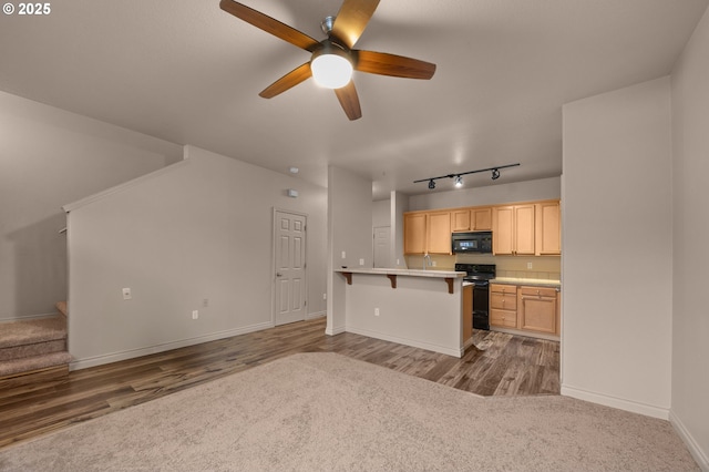 kitchen featuring light wood finished floors, light countertops, light brown cabinets, black appliances, and a kitchen bar