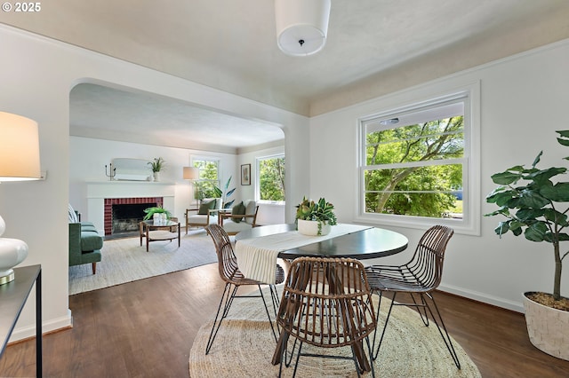 3575 NE Emerson St, Portland, OR 97211 - dining space with arched walkways, dark wood-style flooring, baseboards, and a brick fireplace