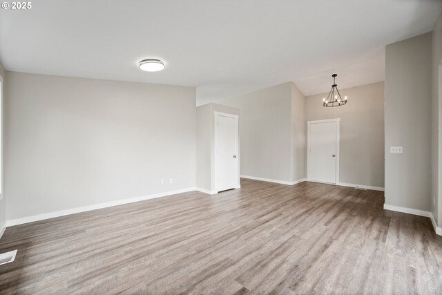 unfurnished room with an inviting chandelier, baseboards, wood finished floors, and visible vents