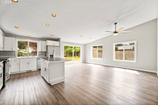 kitchen featuring wood finished floors, a kitchen island, open floor plan, ceiling fan, and appliances with stainless steel finishes