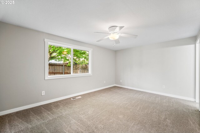empty room with carpet floors, baseboards, ceiling fan, and visible vents