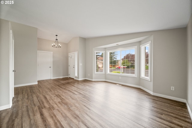 unfurnished living room with an inviting chandelier, baseboards, wood finished floors, and lofted ceiling
