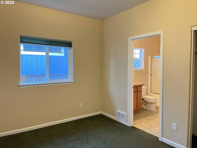 unfurnished bedroom featuring dark carpet and connected bathroom