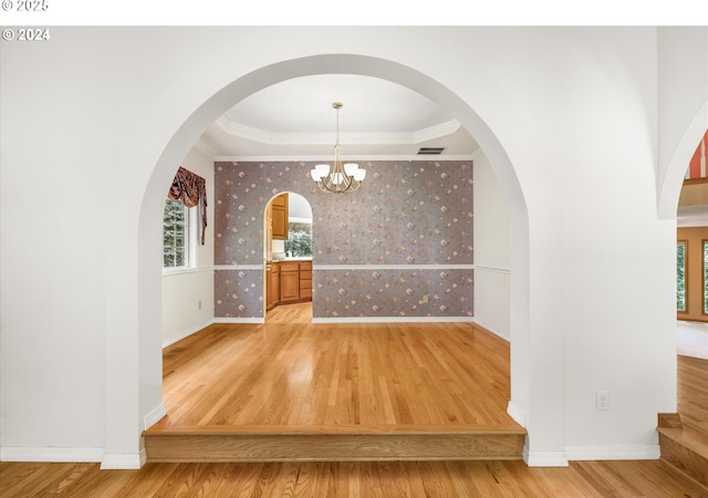 unfurnished dining area with a tray ceiling, an inviting chandelier, hardwood / wood-style flooring, and a healthy amount of sunlight